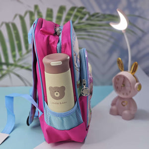 Pink backpack with a bear-themed water bottle on a light blue surface with a decorative plant in the background.