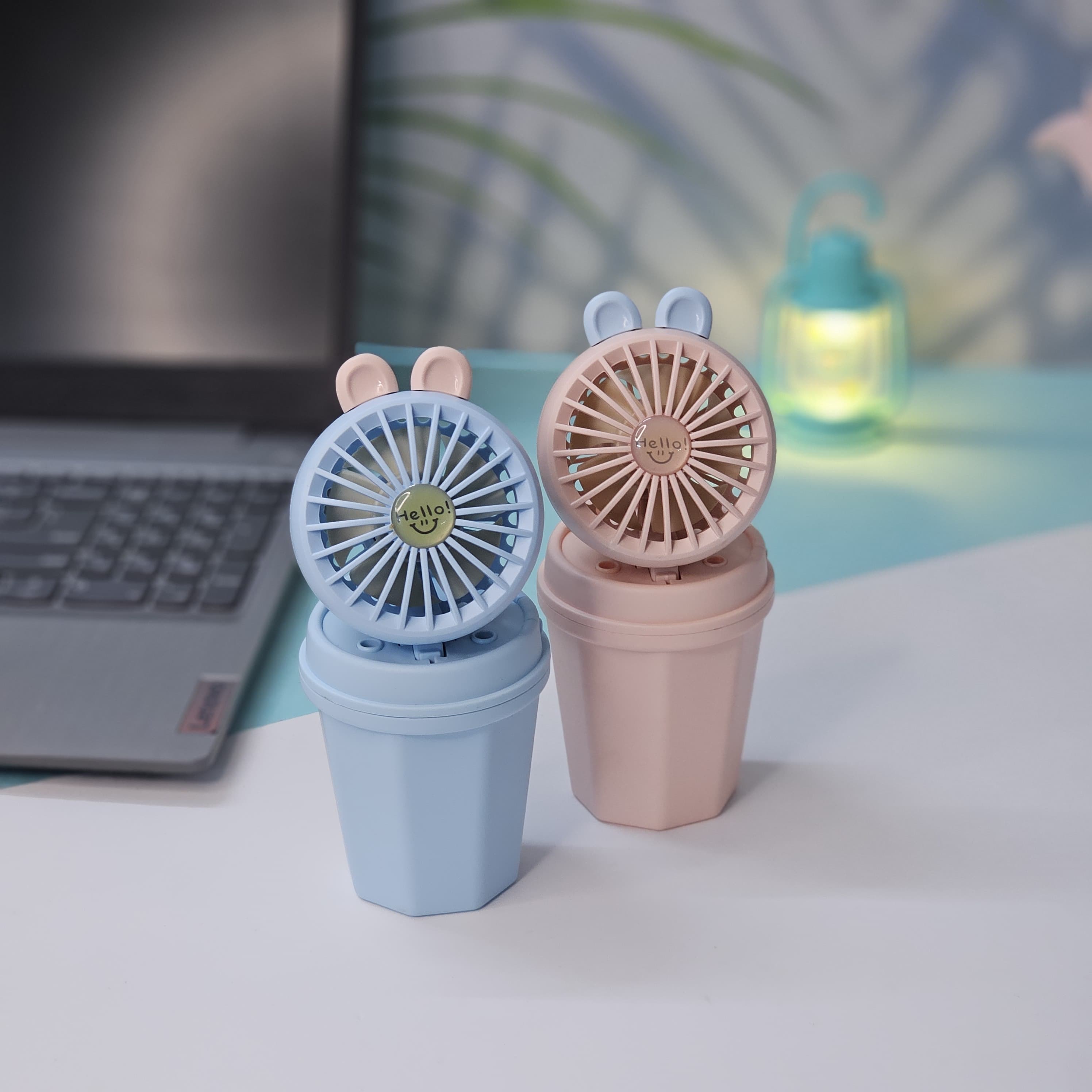 Pair of Usmile Toys hi-speed kids desk fans in light blue and pink, each featuring cute bunny ears and a 'hello' design on the grille, ideal for a child's personal space." www.usmile.toys