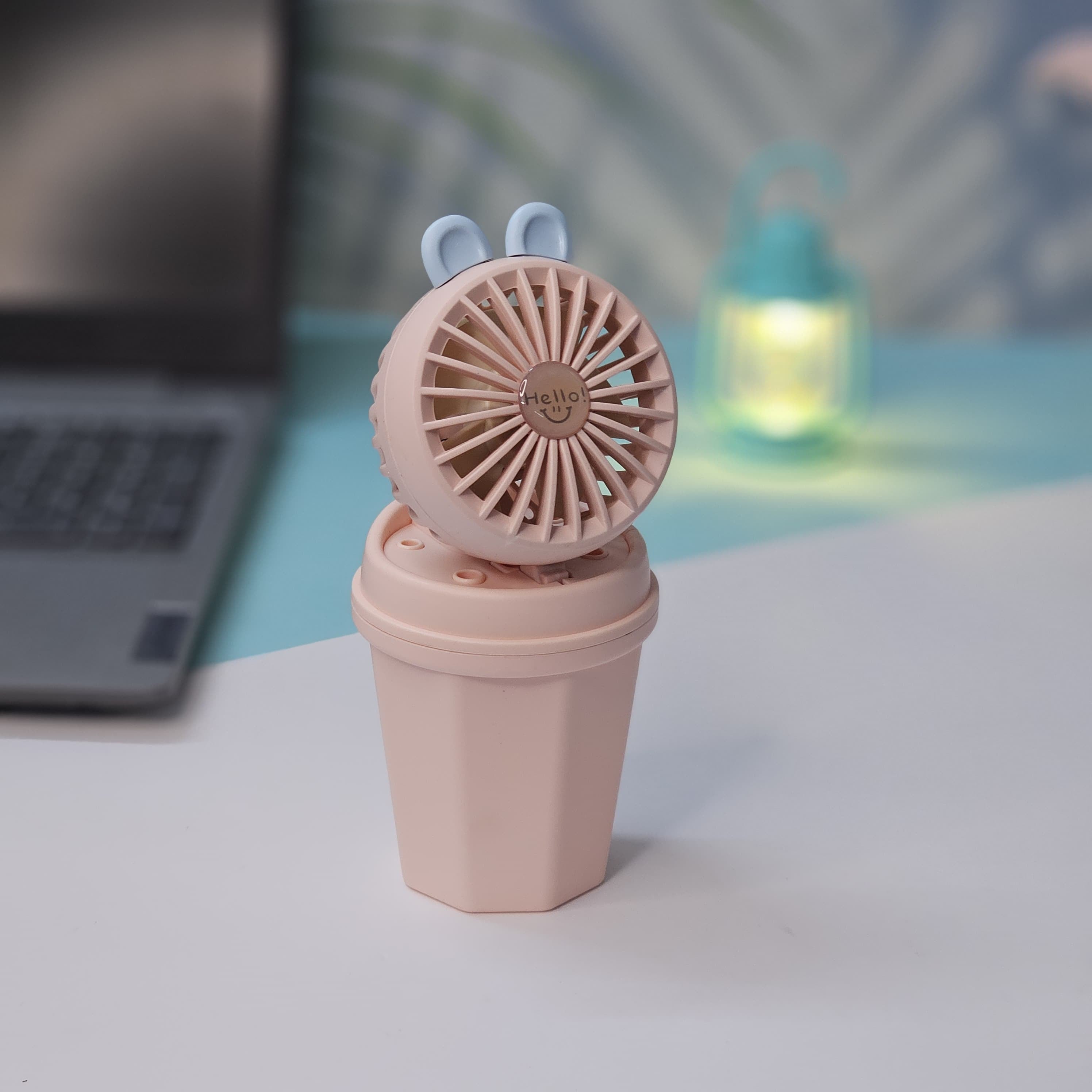 Front view of two Usmile Toys Hi Speed Kids Desk Fans, a blue and a pink one, showing their round grilles with a 'hello' emoji and charming bunny ears, suitable for adding a breeze and fun to any desk."