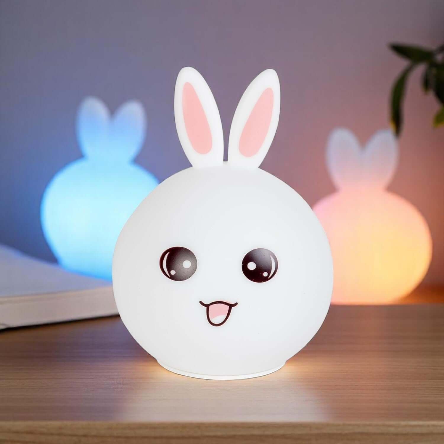 Cute white silicone rabbit night light with pink ears and an adorable face, glowing softly. In the background, two more rabbit lamps glow blue and orange, showcasing the color-changing feature. Perfect as a bedside lamp or nursery decor for kids and adults, providing comforting illumination. www.usmile.com