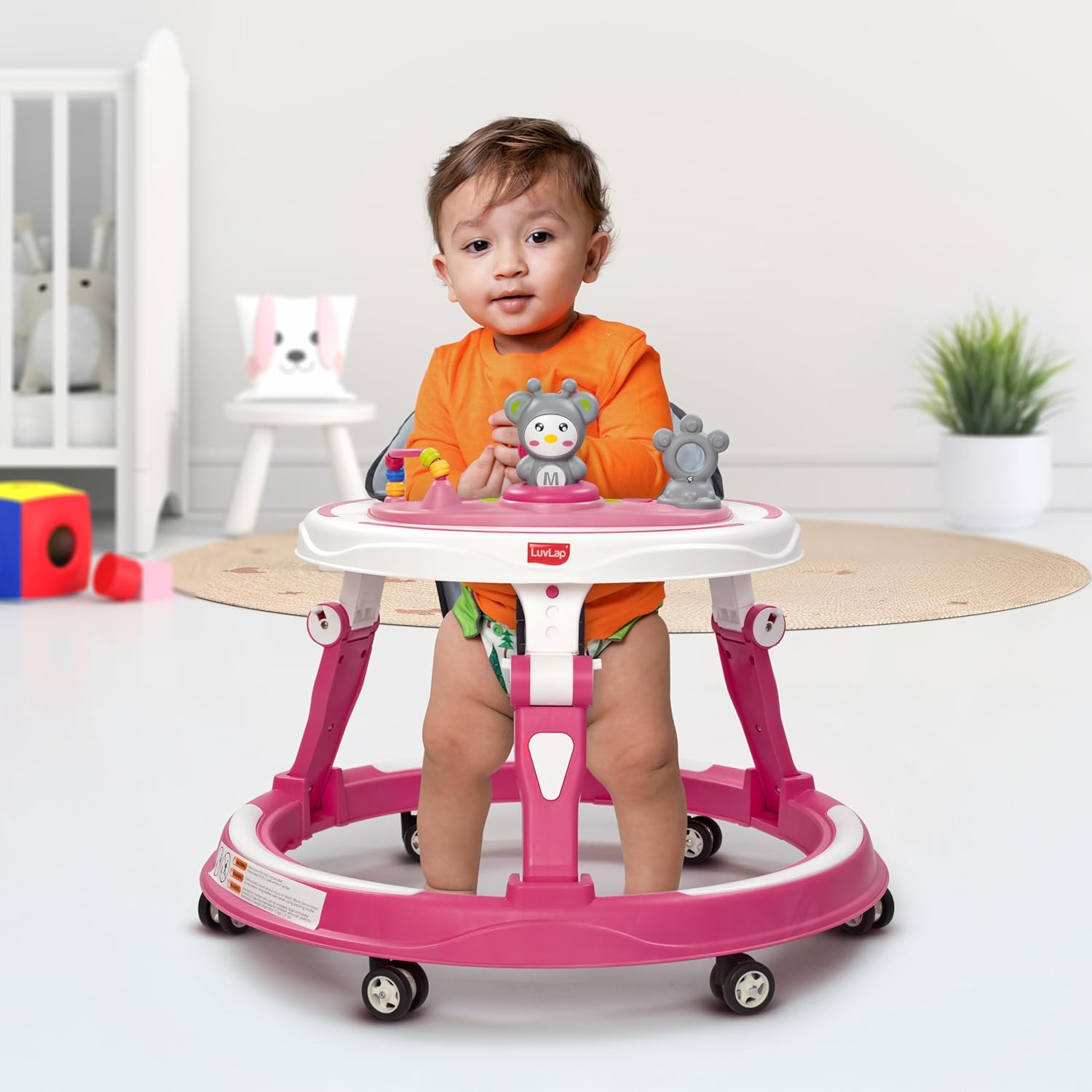 LuvLap 360° Joy baby walker in pink and white, featuring a comfortable gray padded seat, multi-level height adjustment, and engaging toys on the activity tray for infants 9+ months.  www.usmile.toys