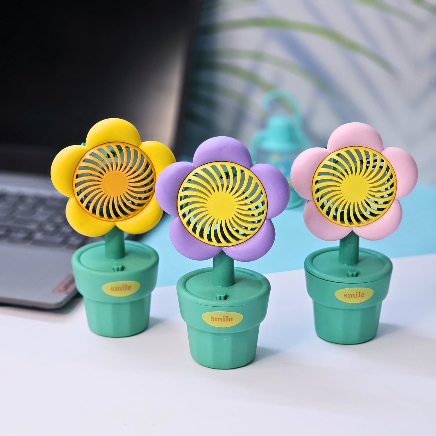 Set of three Usmile Toys flower-shaped mini desk fans in yellow, purple, and pink, each in a green pot with 'smile' text, perfect for kids' rooms or desks."  www.usmile.toys
