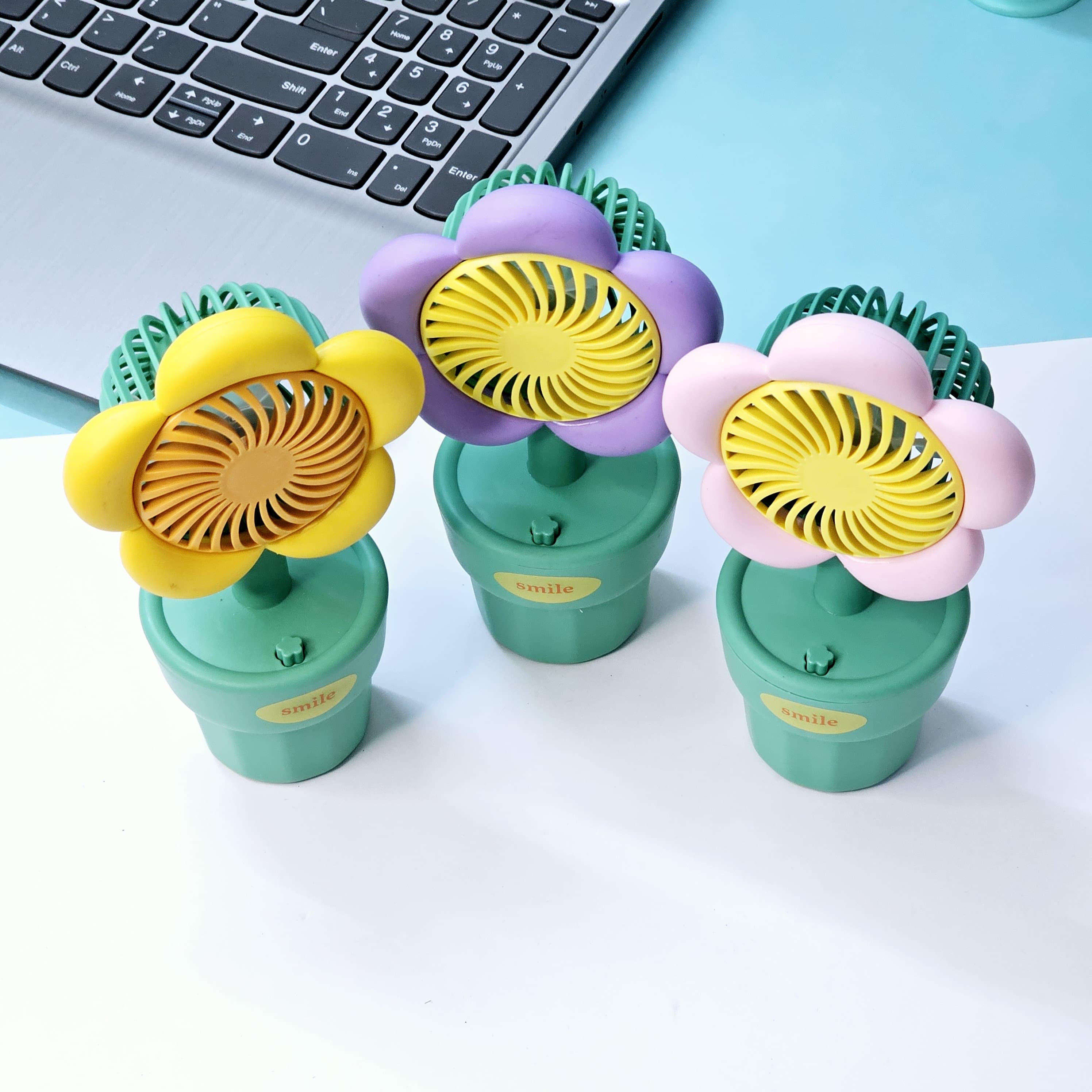 Front view of three Usmile Toys flower-shaped portable fans, featuring colorful petals and a 'smile' engraved green pot base, ideal for children. www.usmile.toys