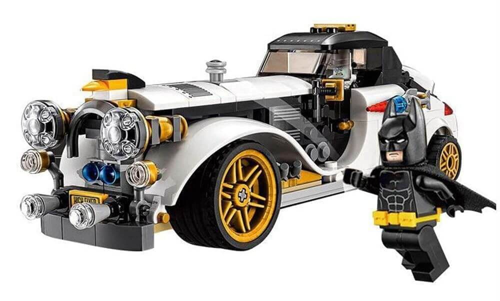 Lego-style building block set featuring a white classic car with gold wheels, Batman minifigure flying above, and Batarang accessory. Perfect for kids to assemble superhero adventures. www.usmile.toys