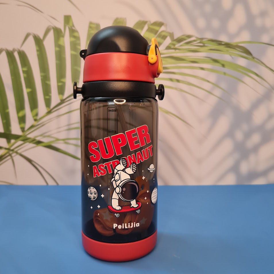 600ml astronaut-themed water bottle for kids featuring a leak-proof design and one-touch flip-open lid. The bottle has a transparent body with space and cartoon graphics, including the word 'SUPER' and an astronaut illustration. The cap is shown in a close-up inset, highlighting the one-key button for opening. The bottle is partially submerged in splashing water, emphasizing its leakproof and durable quality. Available in random colors, ideal for school or travel use