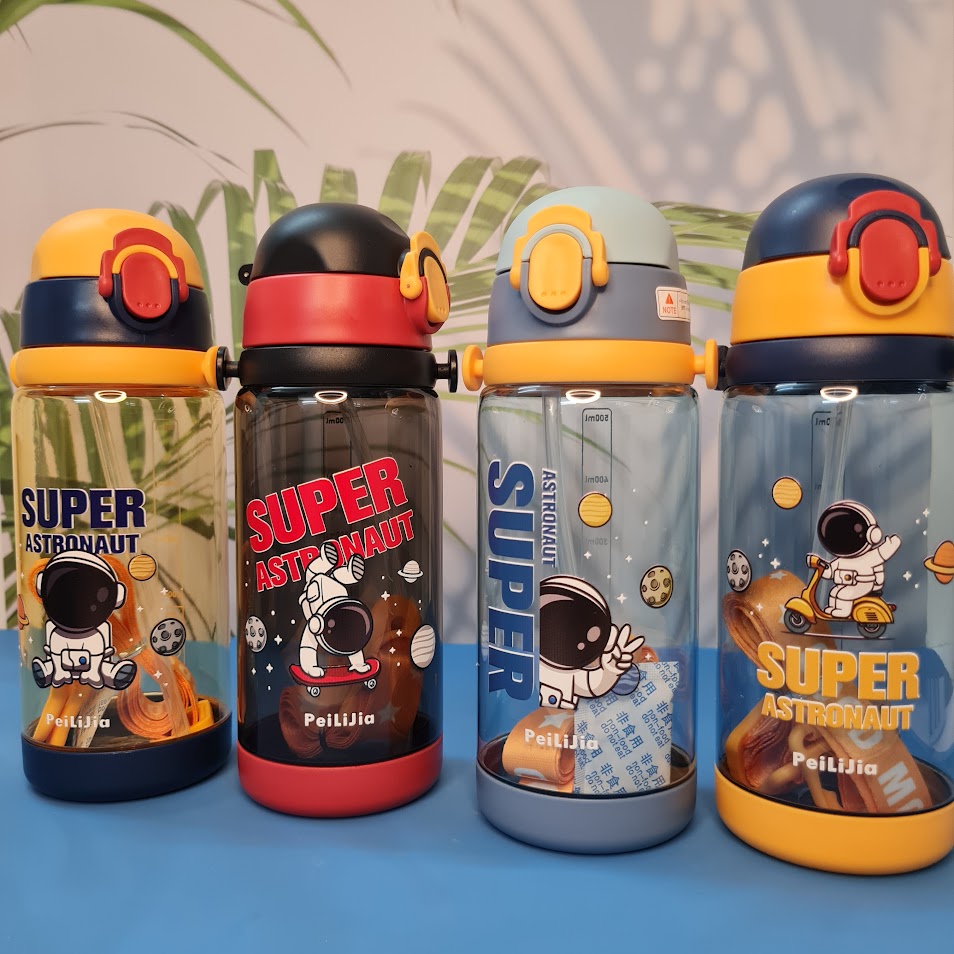 600ml astronaut-themed water bottle for kids featuring a leak-proof design and one-touch flip-open lid. The bottle has a transparent body with space and cartoon graphics, including the word 'SUPER' and an astronaut illustration. The cap is shown in a close-up inset, highlighting the one-key button for opening. The bottle is partially submerged in splashing water, emphasizing its leakproof and durable quality. Available in random colors, ideal for school or travel use