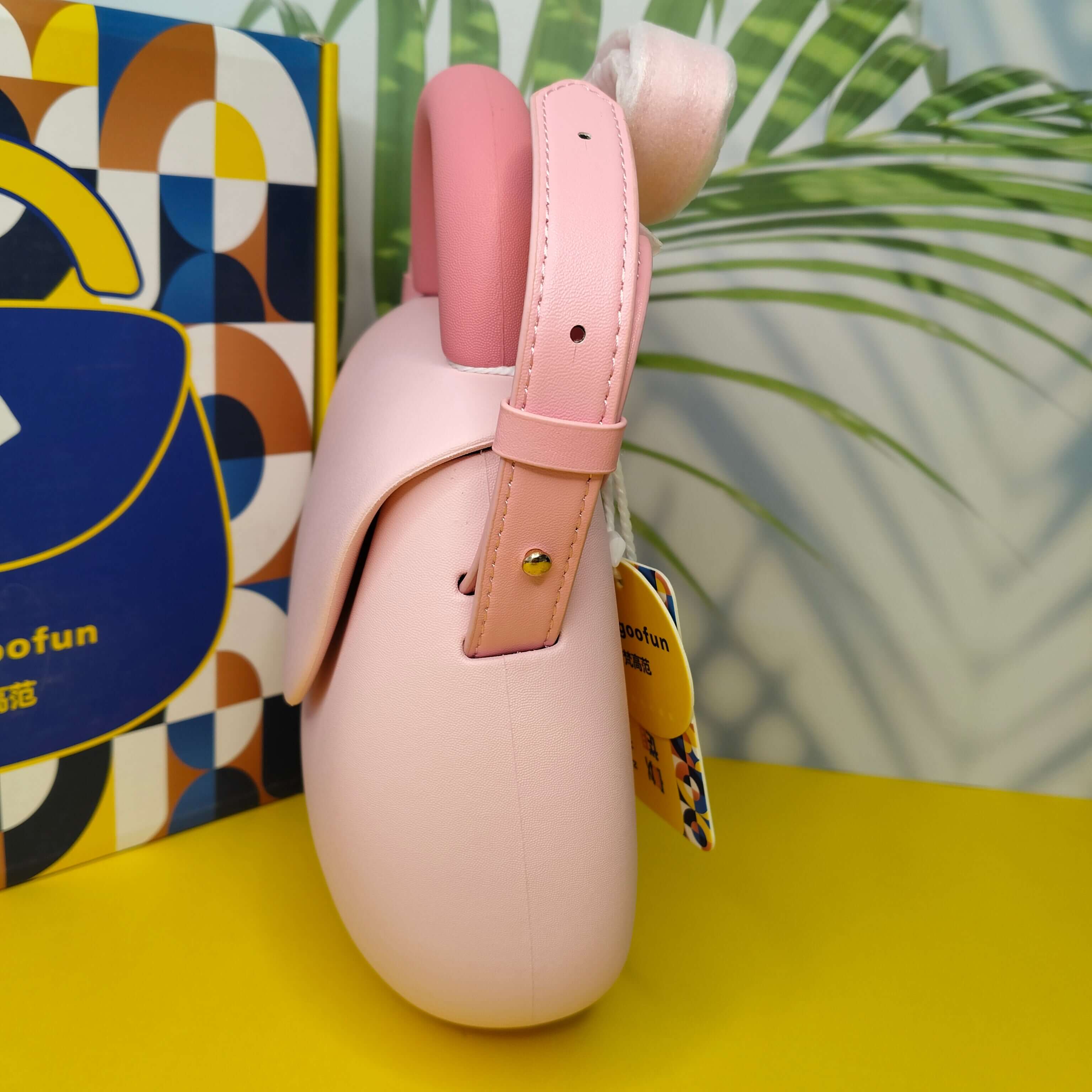 Pink dog muzzle with a tag on a yellow surface with a colorful box and green leaves in the background