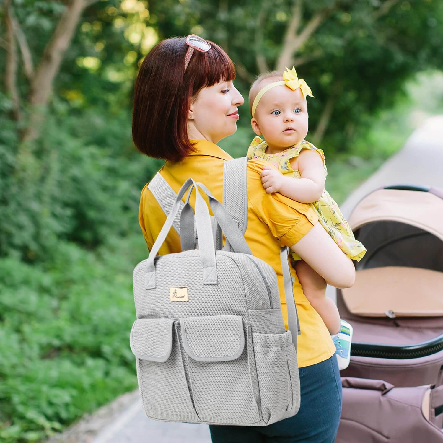 Woman carrying a baby and a gray backpack outdoors