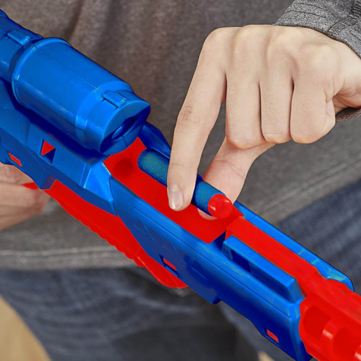 Red and blue toy gun with a person's hand holding it, blurred background