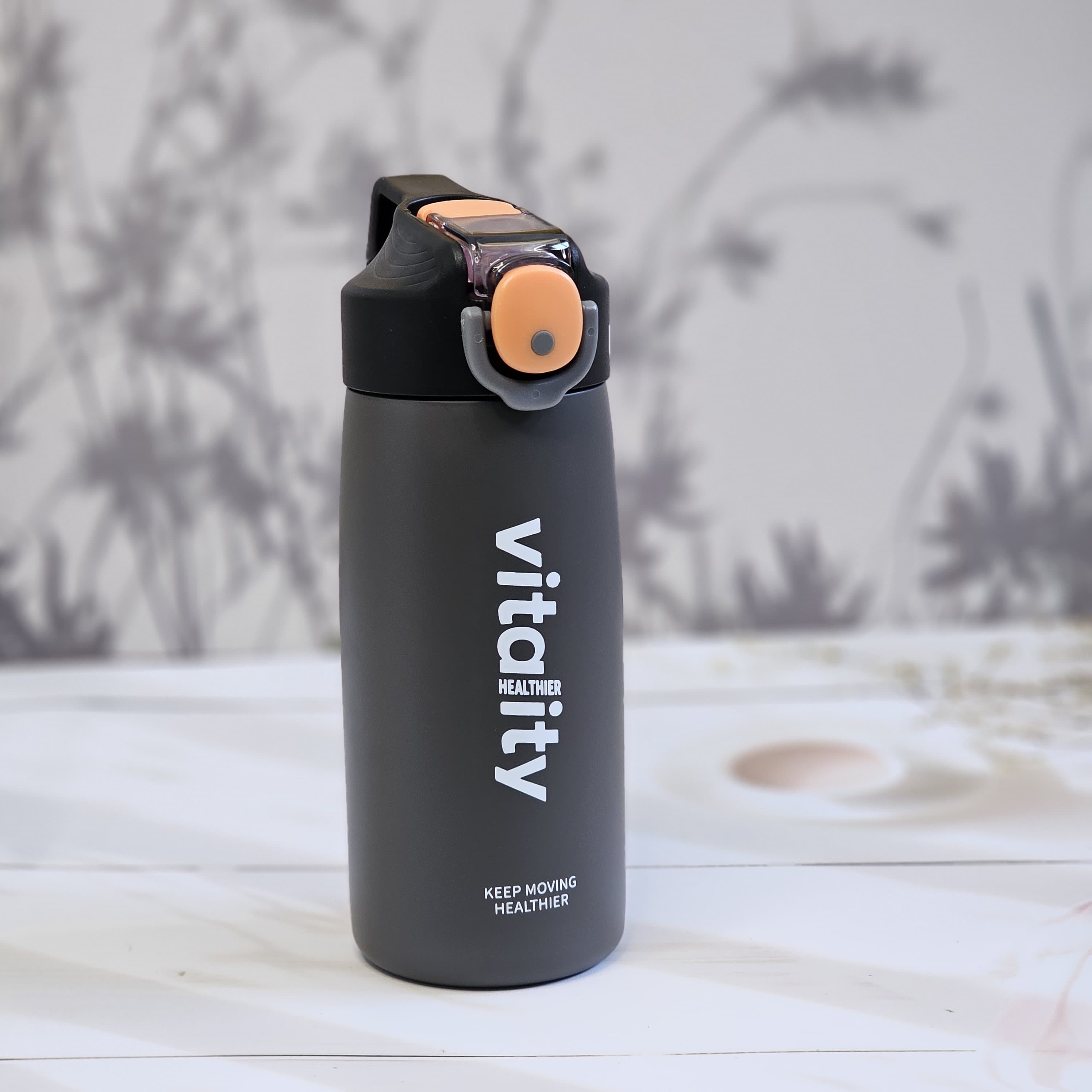 Three stainless steel insulated water bottles in black, white, and pink, showcasing the flip-top lids, 'vitality' branding, and 'keep moving healthier' text, designed for both hot and cold beverages.               www.usmile.toys