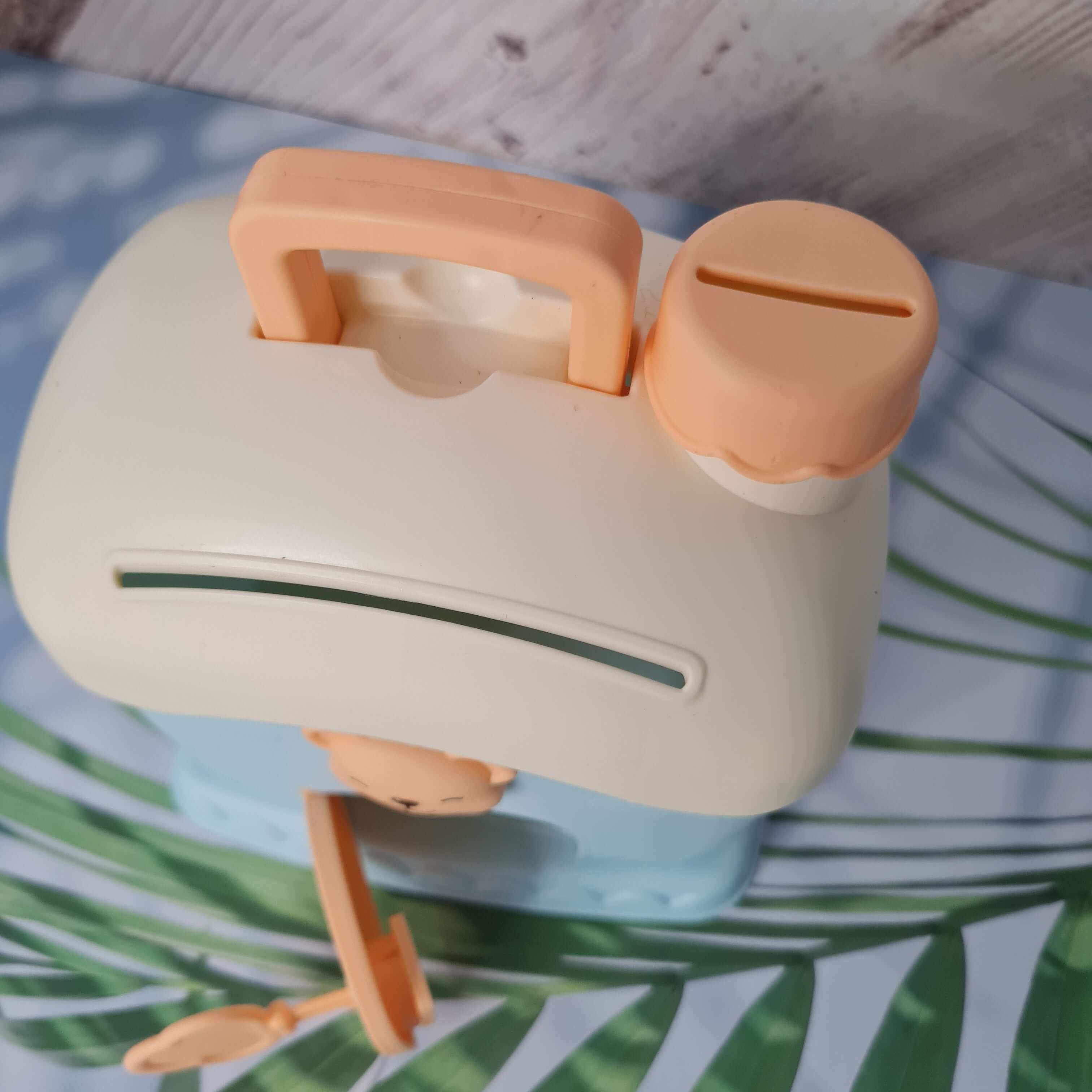 White and peach-colored hair straightener on a surface with green leafy background