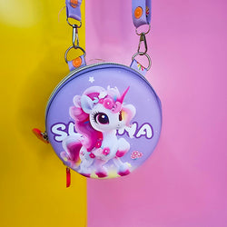 Two colorful, round kids’ sling pouches with attached lanyards are placed on a sandy beige background with a tropical leaf shadow. The left pouch is purple and features an adorable cartoon unicorn with a pink mane, large sparkling eyes, and the name "SHYAMA" written in white. It has a lilac lanyard decorated with candy prints. The right pouch is bright blue with a fierce green cartoon T-Rex dinosaur illustration labeled “DINOSAURS” in bold yellow text. Its lanyard is blue with black dinosaur silhouettes. Bo