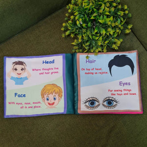 A "My Amazing Body: Head to Toe" fabric book by Kidogen, showing a cartoon child meditating with illustrations of body parts and organs around them.