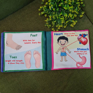 A "My Amazing Body: Head to Toe" fabric book by Kidogen, showing a cartoon child meditating with illustrations of body parts and organs around them.