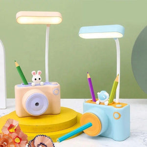 "Two cute camera-shaped study desk LED lamps for kids, one peach and one light blue, each featuring a pencil holder and a built-in pencil sharpener. Ideal for reading and organizing stationery from uSmile.toys." www.usmile.toys