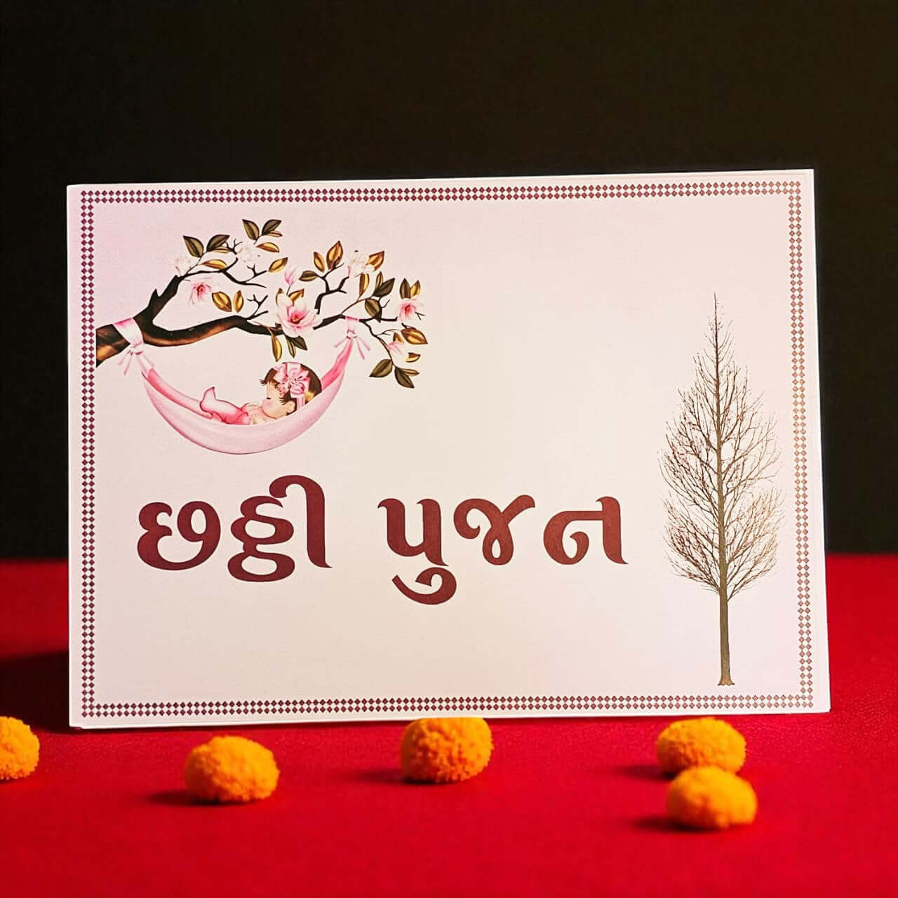 Card with a baby in a hammock and tree design, placed on a red surface with decorative items.
