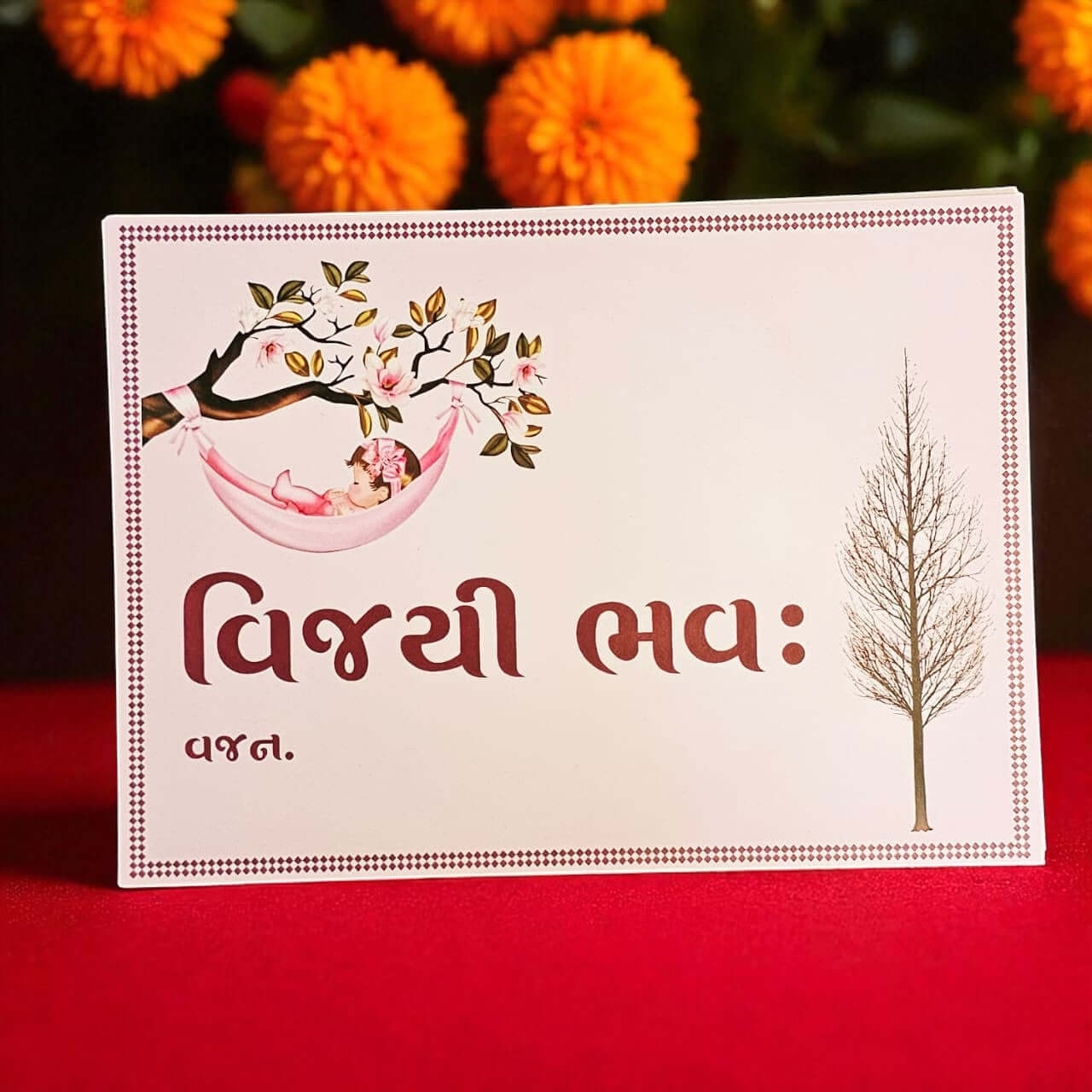 Card with illustrations of a baby in a hammock and a tree, on a red background with orange flowers.