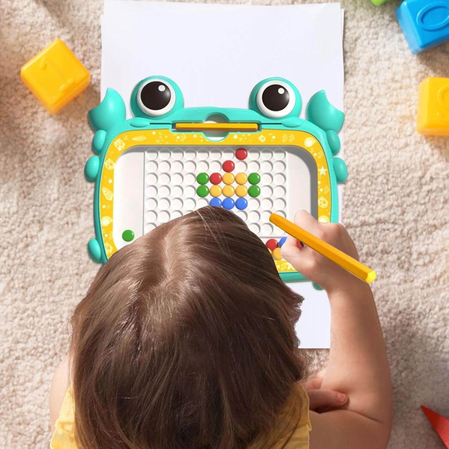 Child using a colorful drawing toy with magnetic letters on a carpeted floor.