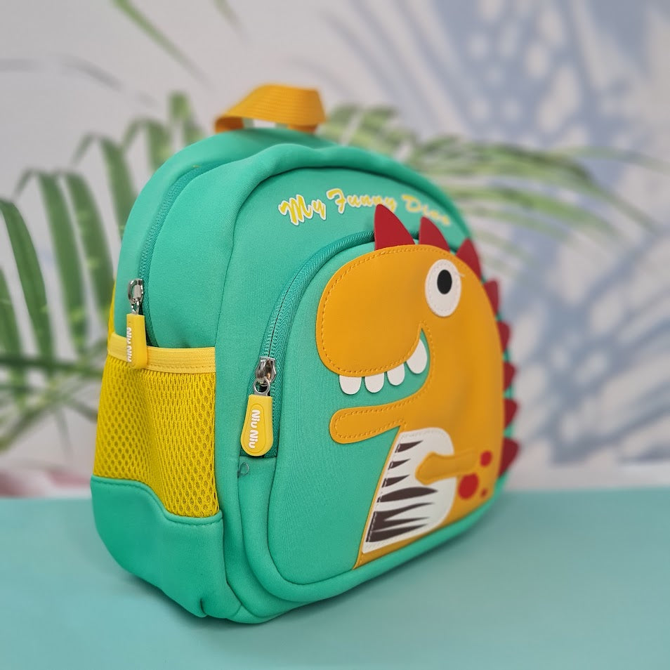 Small, teal backpack for children featuring a large orange dinosaur applique with red spikes and white teeth on the front pocket. Above the dinosaur is embroidered teal cursive text that reads "My Funny Dino". The backpack has yellow straps and yellow mesh side pockets