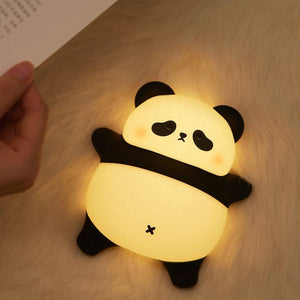 Adorable glowing white and black silicone night lamp for kids, shaped like a cute lying panda, illuminating a surface. Ideal for a comforting and soft light in a child's bedroom from uSmile.toys." www.usmile.toys
