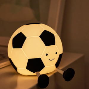 Adorable glowing white and black silicone night lamp for kids, shaped like a soccer ball (football) with a friendly smiley face and small legs, resting on a surface. Ideal for a sports-themed bedroom from uSmile.toys." www.usmile.toys
