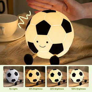 Adorable glowing white and black silicone night lamp for kids, shaped like a soccer ball (football) with a friendly smiley face and small legs, resting on a surface. Ideal for a sports-themed bedroom from uSmile.toys." www.usmile.toys