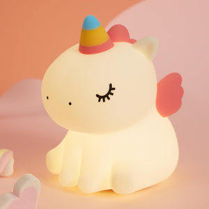 Adorable glowing white silicone night lamp for kids, shaped like a cute sitting unicorn with a colorful horn and pink wings. Provides a soft, comforting light for bedrooms. From uSmile.toys www.usmile.toys
