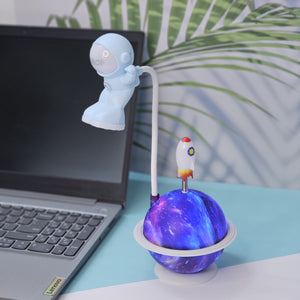 "Usmile Toys unique astronaut desk lamp, featuring a flexible neck, a light-up galaxy planet base, and a small rocket, ideal for a child's bedroom or study area."
