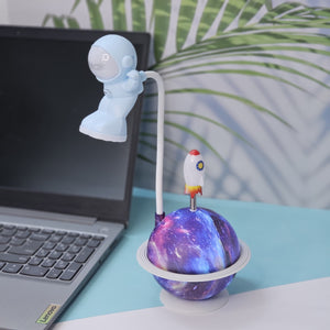 "Usmile Toys unique astronaut desk lamp, featuring a flexible neck, a light-up galaxy planet base, and a small rocket, ideal for a child's bedroom or study area."