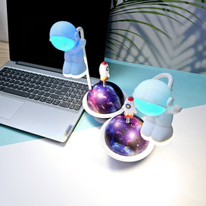 "Close-up of a Usmile Toys creative astronaut lamp, showing its white astronaut figure, flexible arm, and a striking purple and blue glowing planet base with a rocket fin." www.usmile.toys