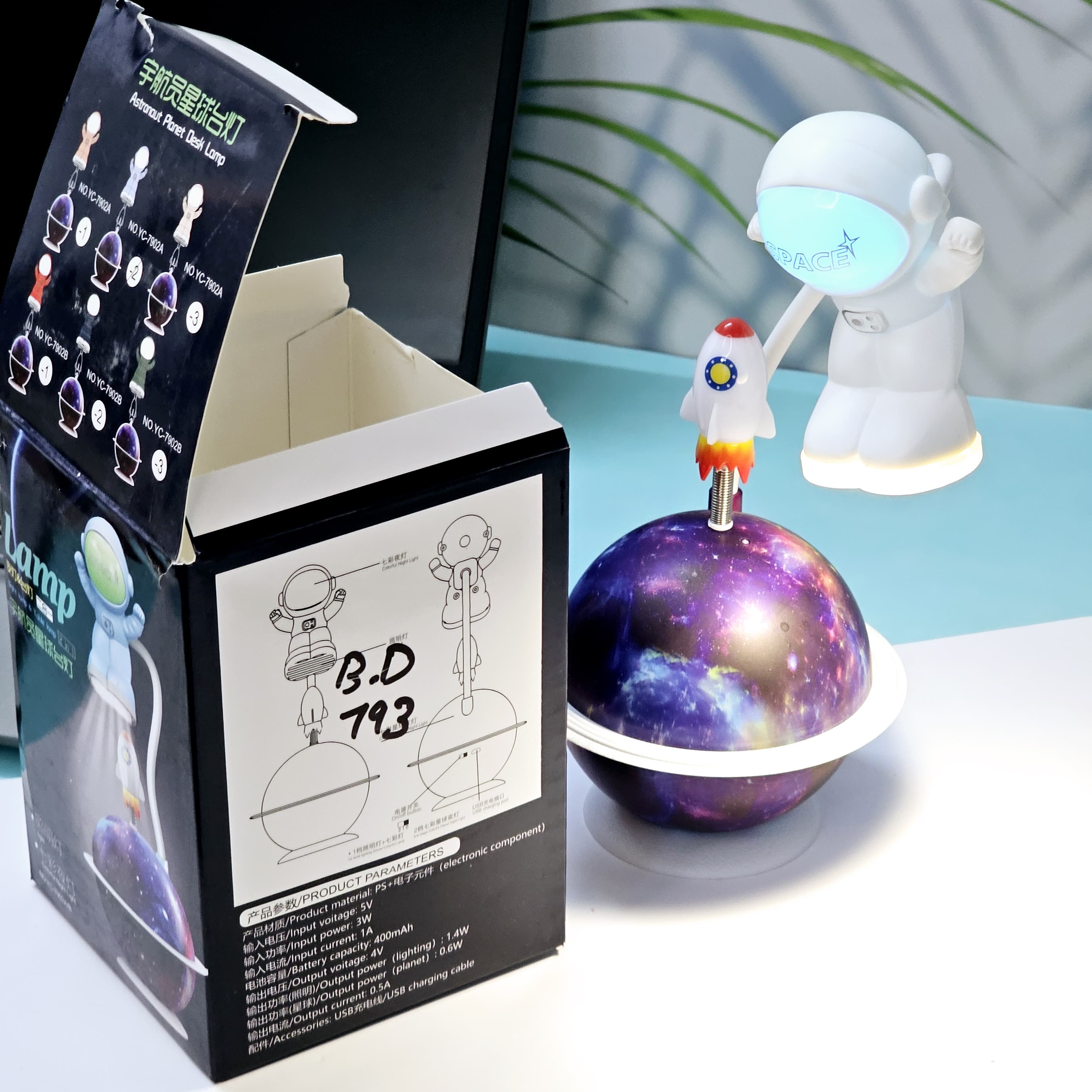 "Close-up of a Usmile Toys creative astronaut lamp, showing its white astronaut figure, flexible arm, and a striking purple and blue glowing planet base with a rocket fin."