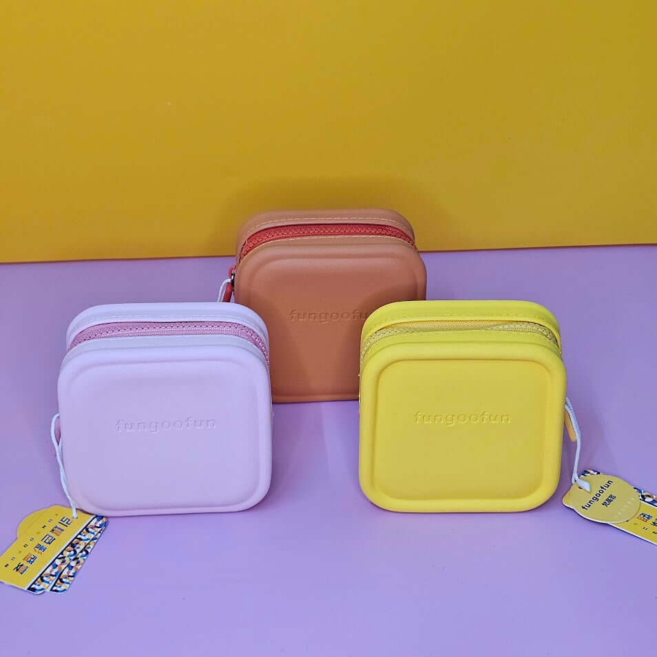 Three small rectangular bags in purple, brown, and yellow on a purple surface with a yellow background.