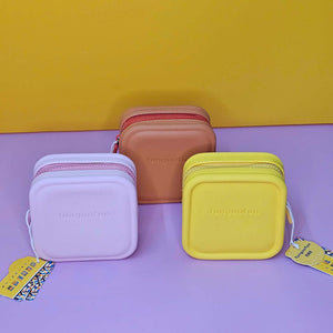 Three small rectangular bags in purple, brown, and yellow on a purple surface with a yellow background.