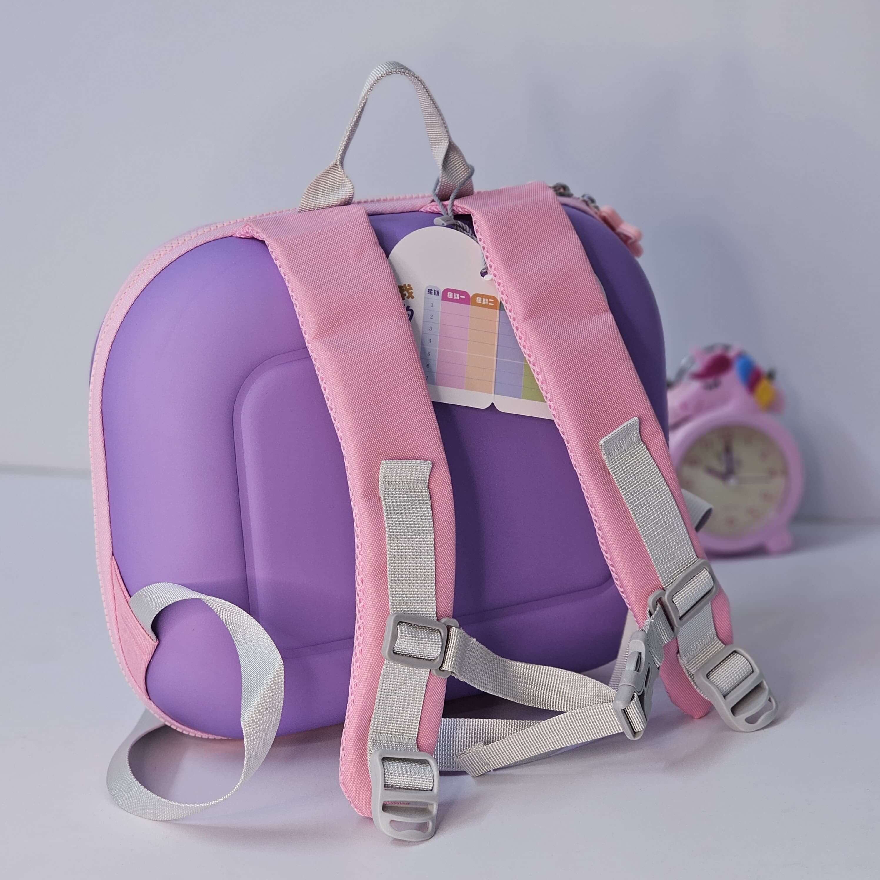 Purple and pink children's backpack with a clock in the background