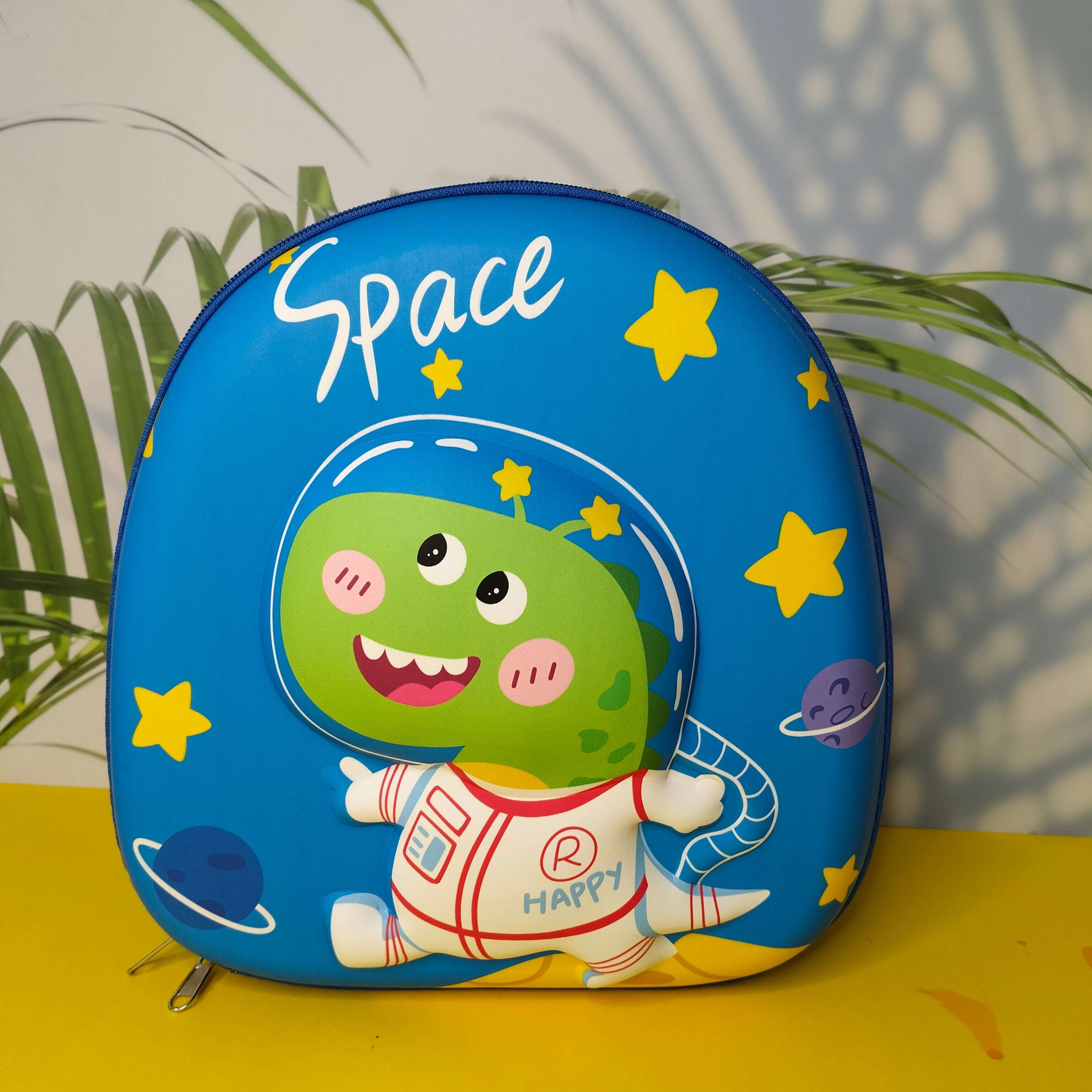 Children's blue bag with cartoon character and 'Space' text on a yellow surface with green plants in the background.