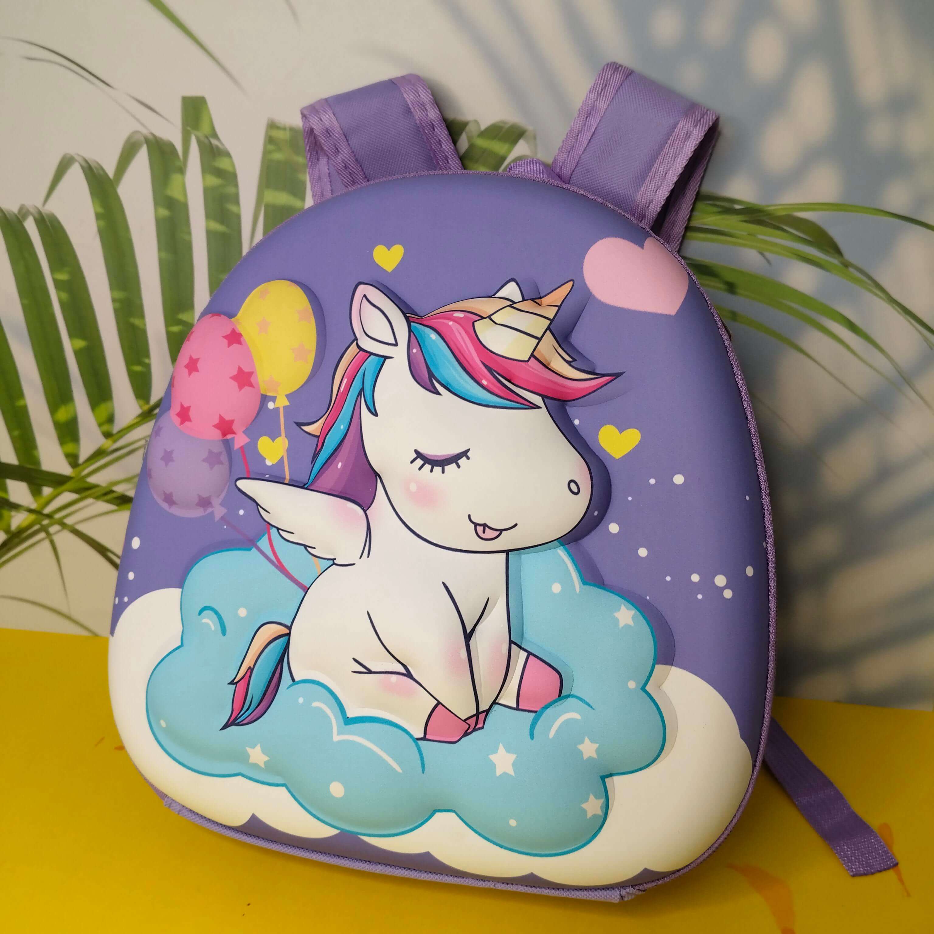 Children's backpack with a unicorn design on a yellow surface with green leaves in the background