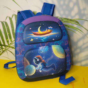 Children's backpack with space-themed design on a yellow surface with green leaves in the background