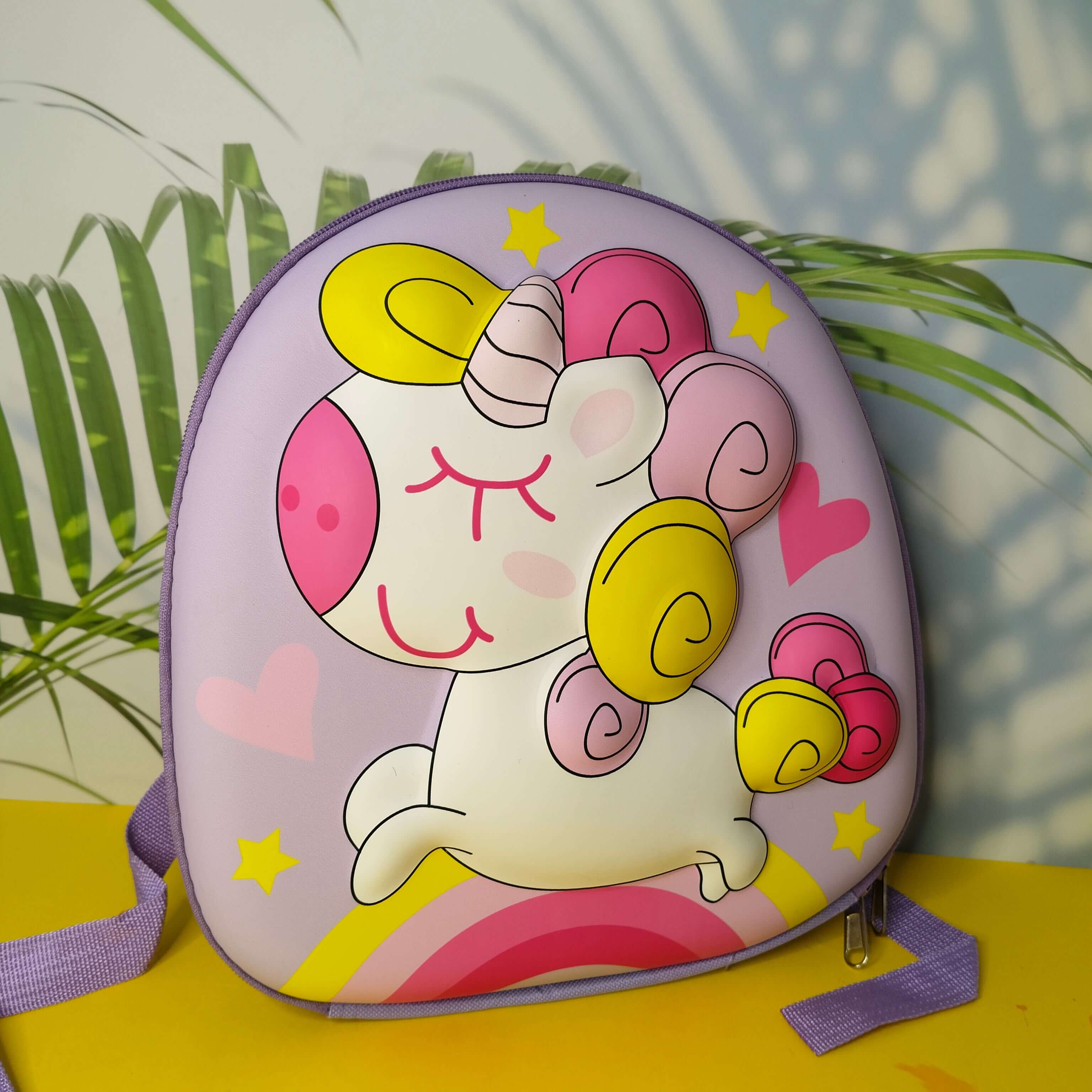 Children's backpack with a unicorn design on a yellow surface with green plants in the background