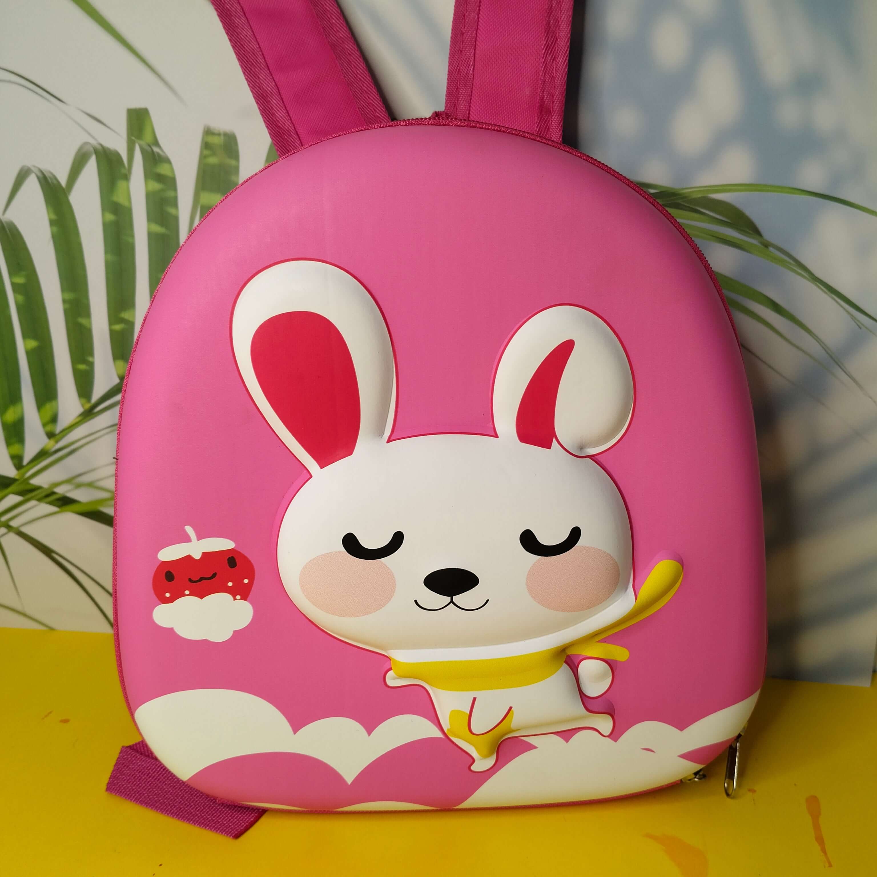 Pink children's backpack with cartoon rabbit design on a yellow surface.