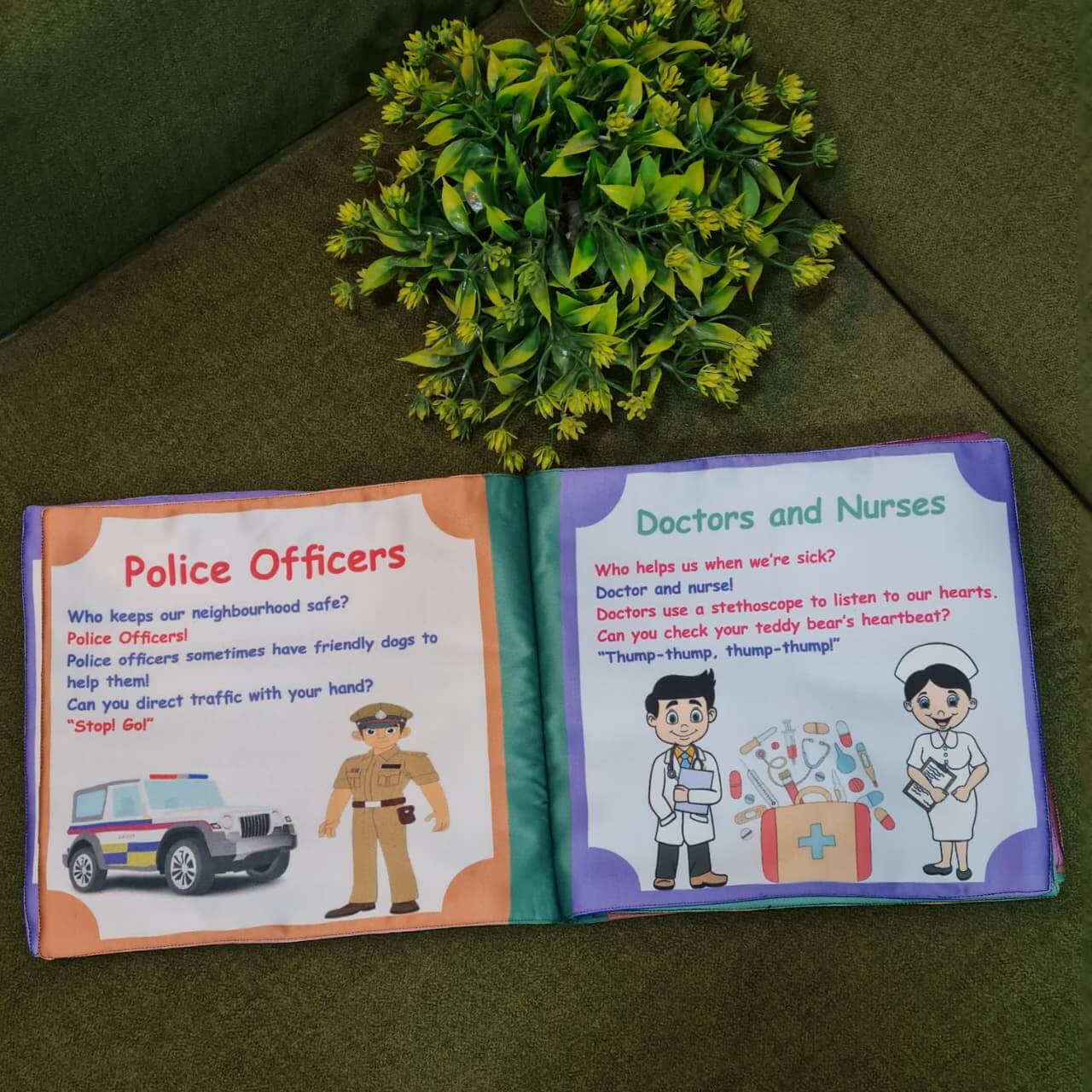 An open "Our Helping Heroes" fabric book by Kidogen, displaying pages about "Police Officers" and "Doctors and Nurses" with illustrations of community helpers and descriptive text.