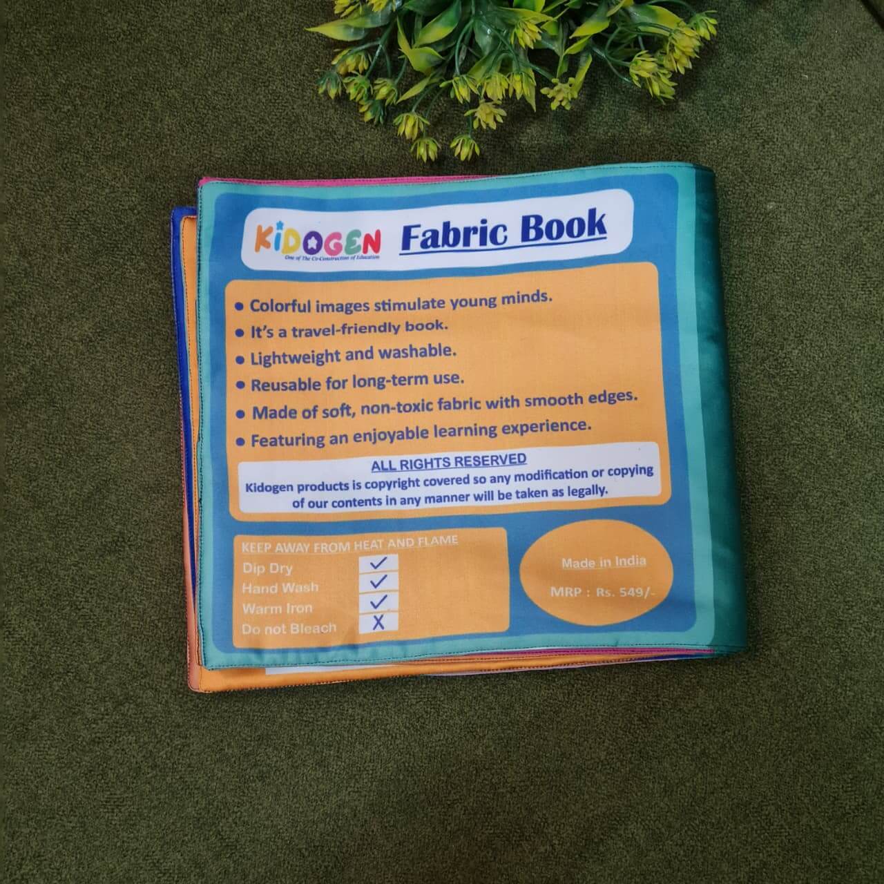 Our Helping Heroes" fabric book by Kidogen, featuring illustrations of a teacher, a farmer, a soldier, a fire truck, and a military vehicle, with the brand logo.