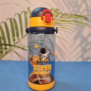600ml astronaut-themed water bottle for kids featuring a leak-proof design and one-touch flip-open lid. The bottle has a transparent body with space and cartoon graphics, including the word 'SUPER' and an astronaut illustration. The cap is shown in a close-up inset, highlighting the one-key button for opening. The bottle is partially submerged in splashing water, emphasizing its leakproof and durable quality. Available in random colors, ideal for school or travel use