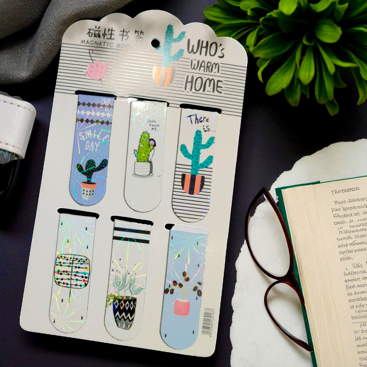 Set of magnetic bookmarks on a card with decorative designs, placed on a surface with a book and glasses.