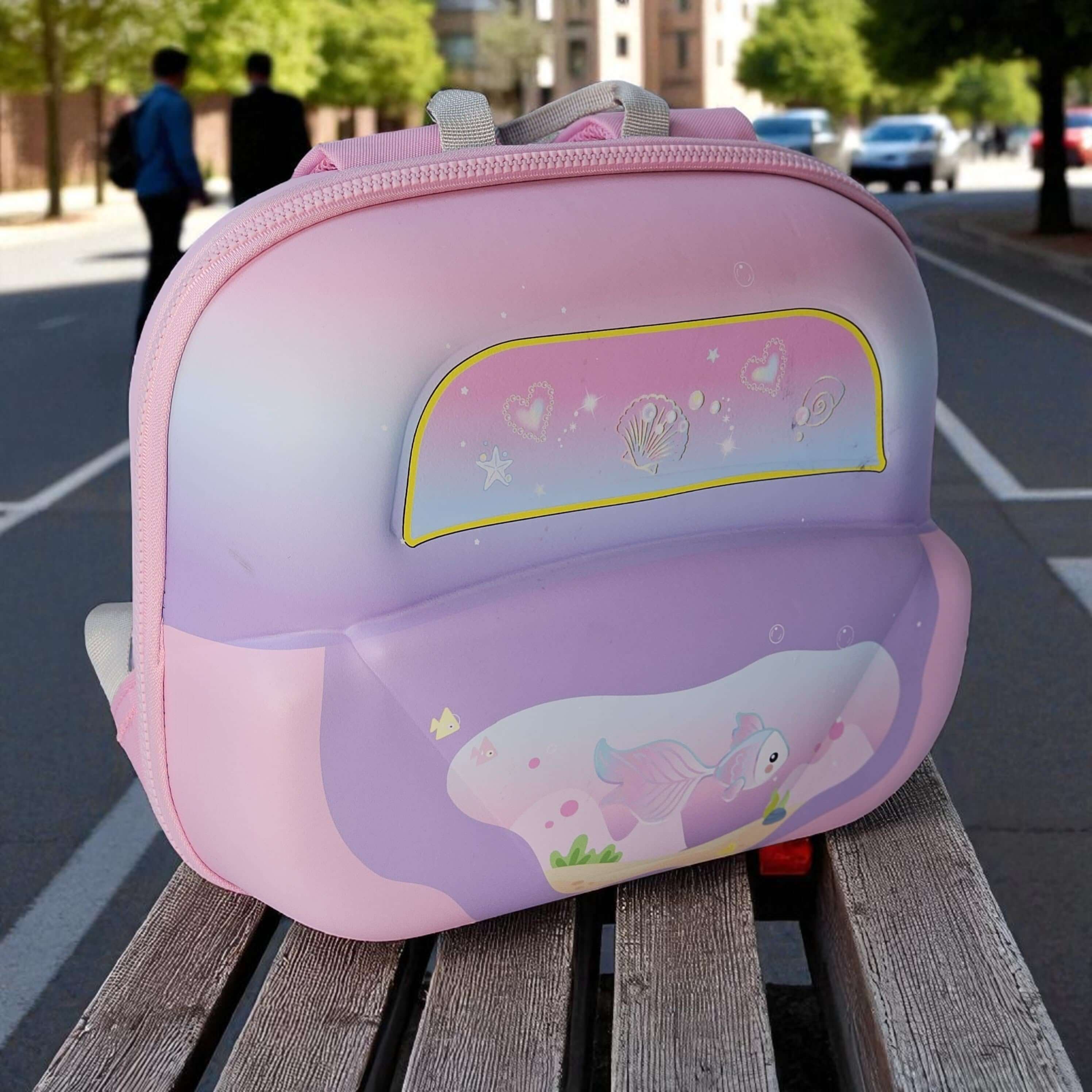 Pink and purple children's backpack with cartoon design on a wooden bench outdoors.