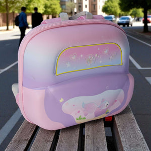 Pink and purple children's backpack with cartoon design on a wooden bench outdoors.
