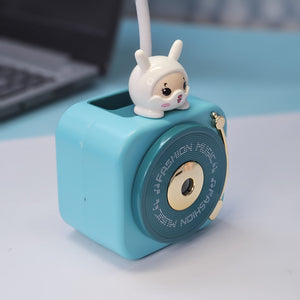 Compact Usmile Toys LED desk lamp with a built-in pencil sharpener and pen holder, perfect for students and kids. This space-saving teal plastic desk light offers bright illumination for reading and drawing, helping children stay organized." www.usmile.toys