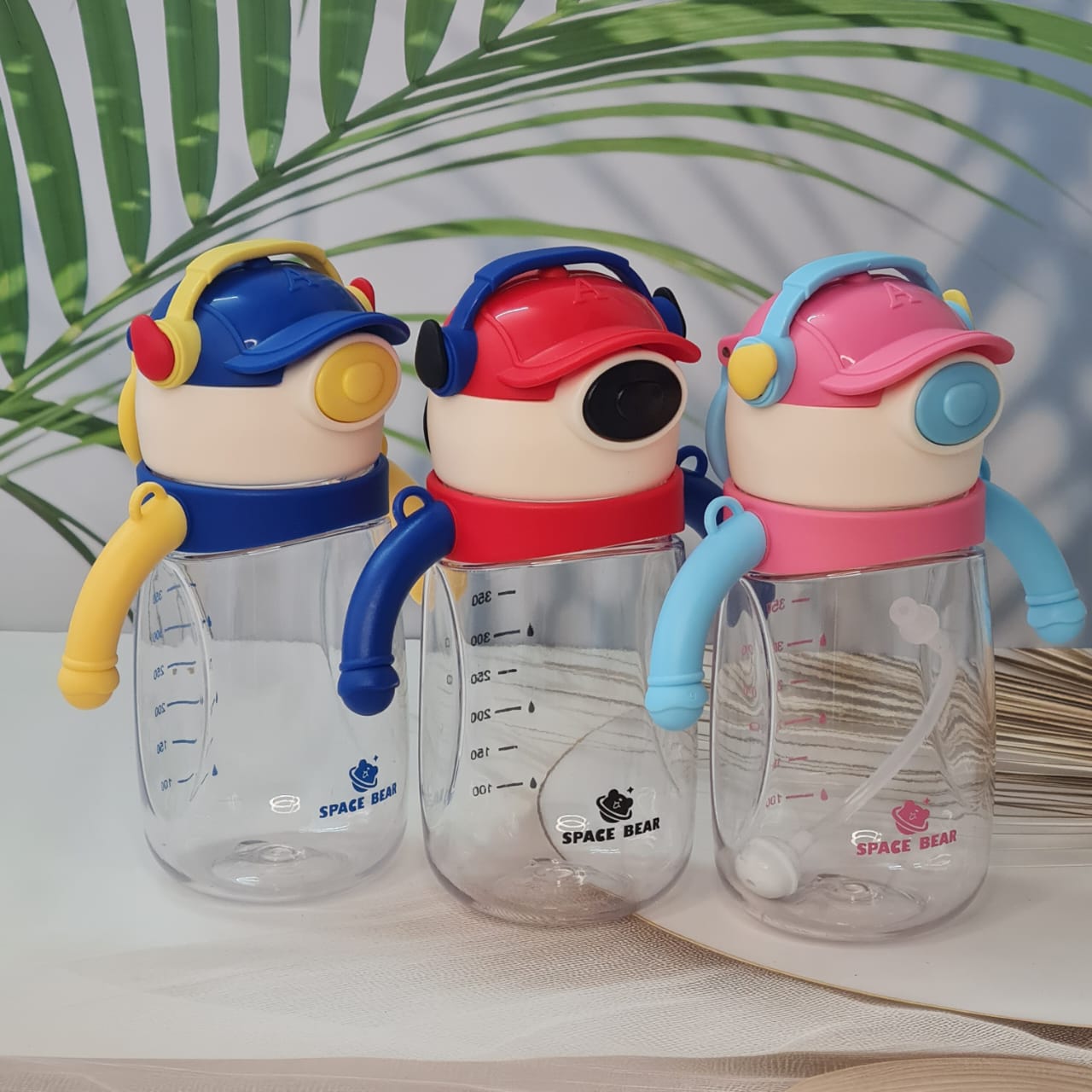 Set of three Space Bear plastic water bottles for kids in blue, red, and pink, each with a straw, handle, and unique bear-themed cap resembling headphones. Ideal sippy cups for toddlers and school children on usmile.toys. www.usmile.toys