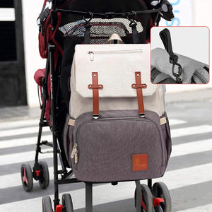 Gray and beige backpack attached to a stroller with close-up of attachment on a blurred background.