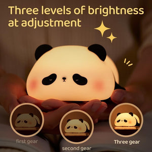 Adorable glowing white and black silicone night lamp for kids, shaped like a cute lying flat panda, resting on green grass against a blue sky. Perfect for a calming bedroom ambiance from uSmile.toys." www.usmile.toys