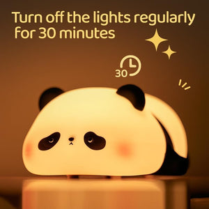 Adorable glowing white and black silicone night lamp for kids, shaped like a cute lying flat panda, resting on green grass against a blue sky. Perfect for a calming bedroom ambiance from uSmile.toys." www.usmile.toys